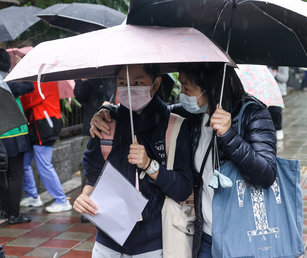 111學年度學科能力測驗22日進入第2天考試,台北市雨勢不斷,家長撐著傘陪同考生前往考場應試,並摟肩為孩子加油打氣。(圖/中央社)