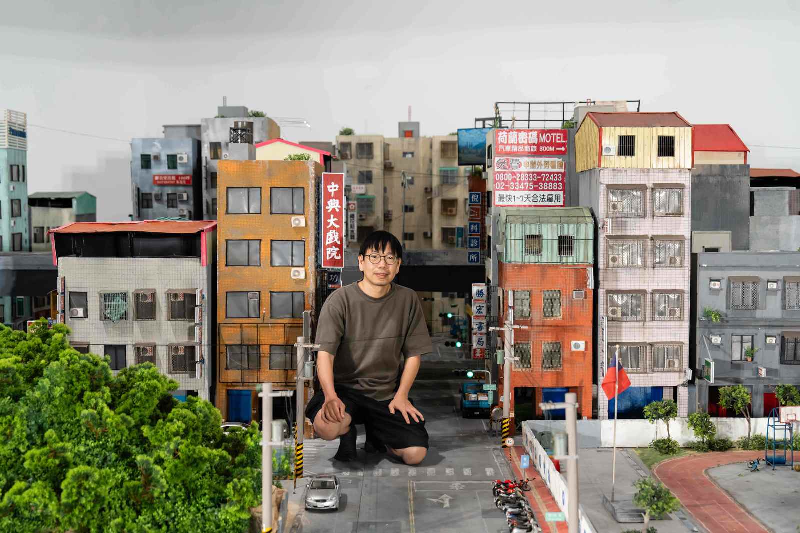張立人與《戰鬥之城》城市模型合影。以自身身體為比例尺、依憑記憶空間尺度搭建展場舞台。(圖/內惟藝術中心)