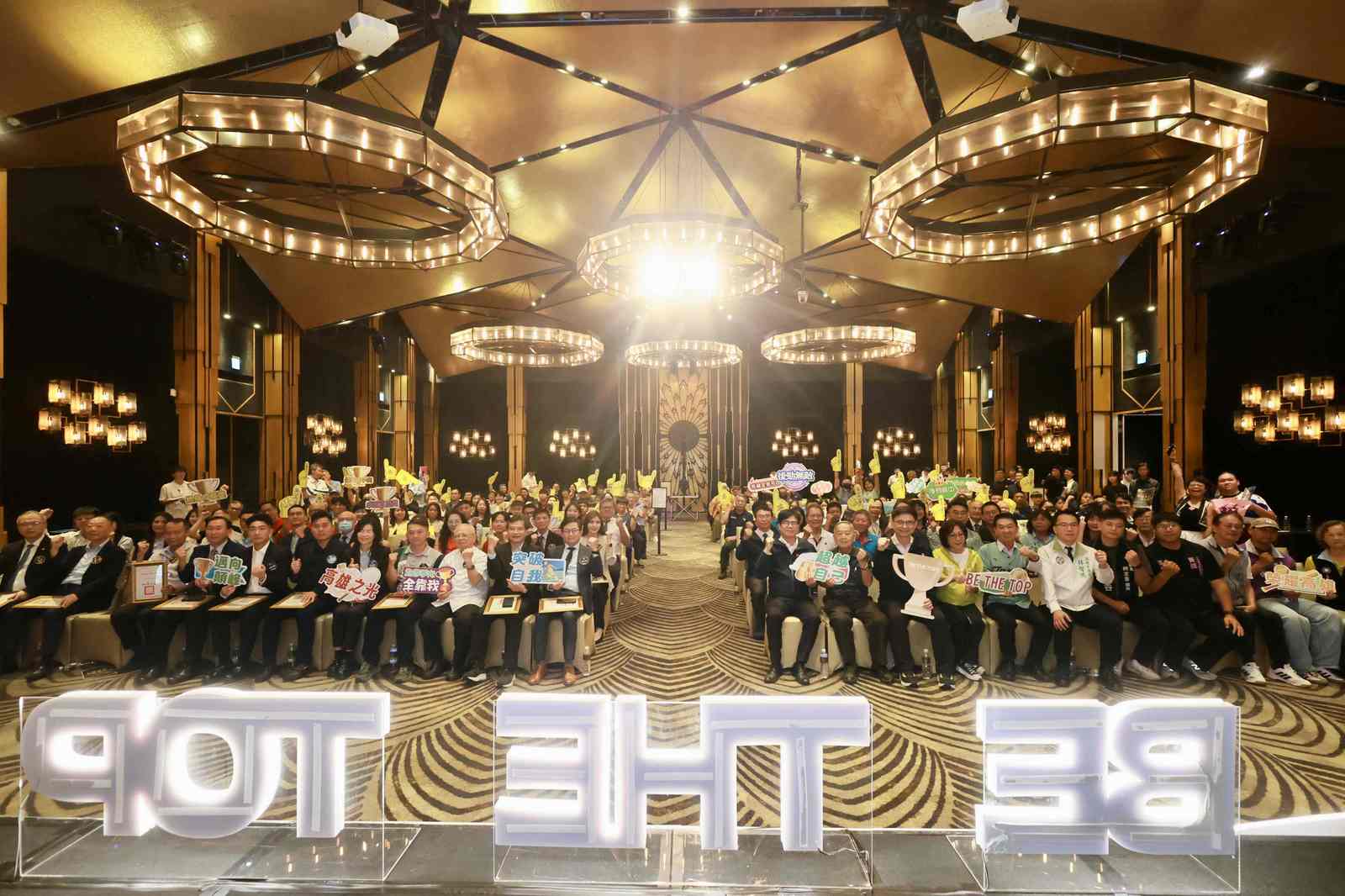 貴賓齊力點亮「BE THE TOP」打氣裝置標語,全體獲獎者台下大合照,展現高雄體育堅強實力。(高雄市政府運發局提供)