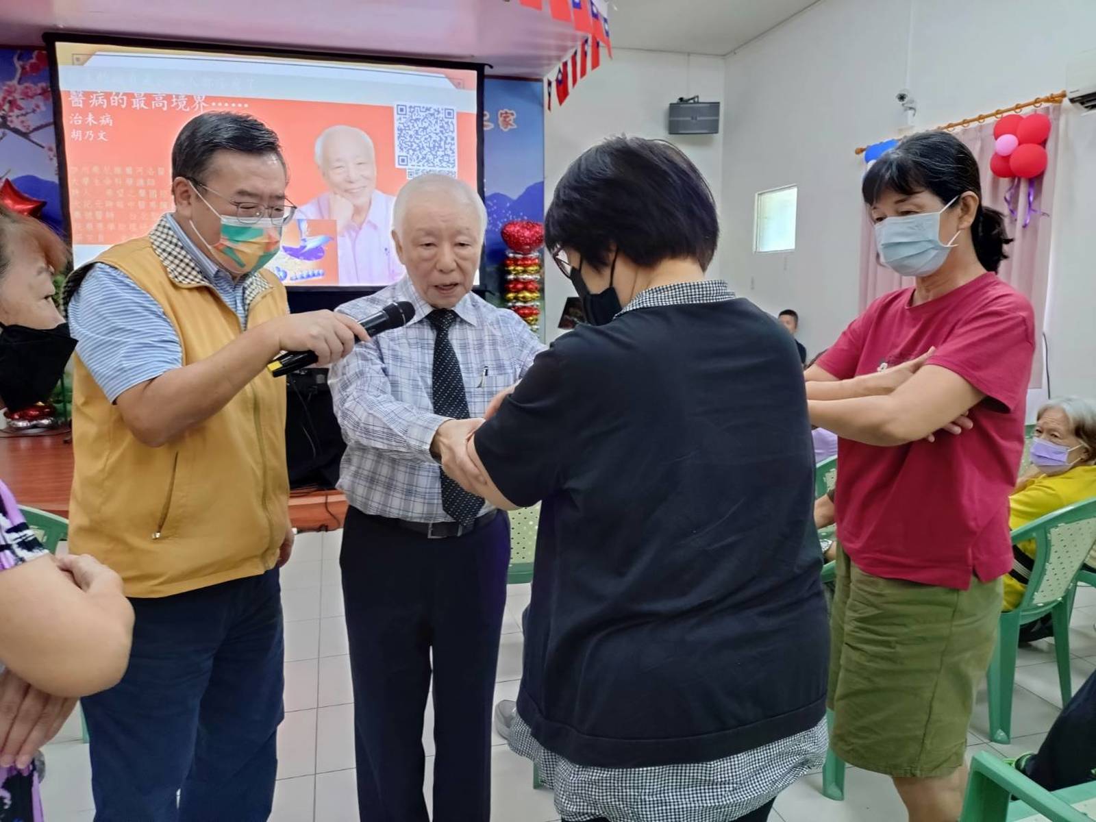 中醫師胡乃文(中)在高雄榮家養生講座中,示範穴位按壓,與現場參與者互動。(圖/新唐人)