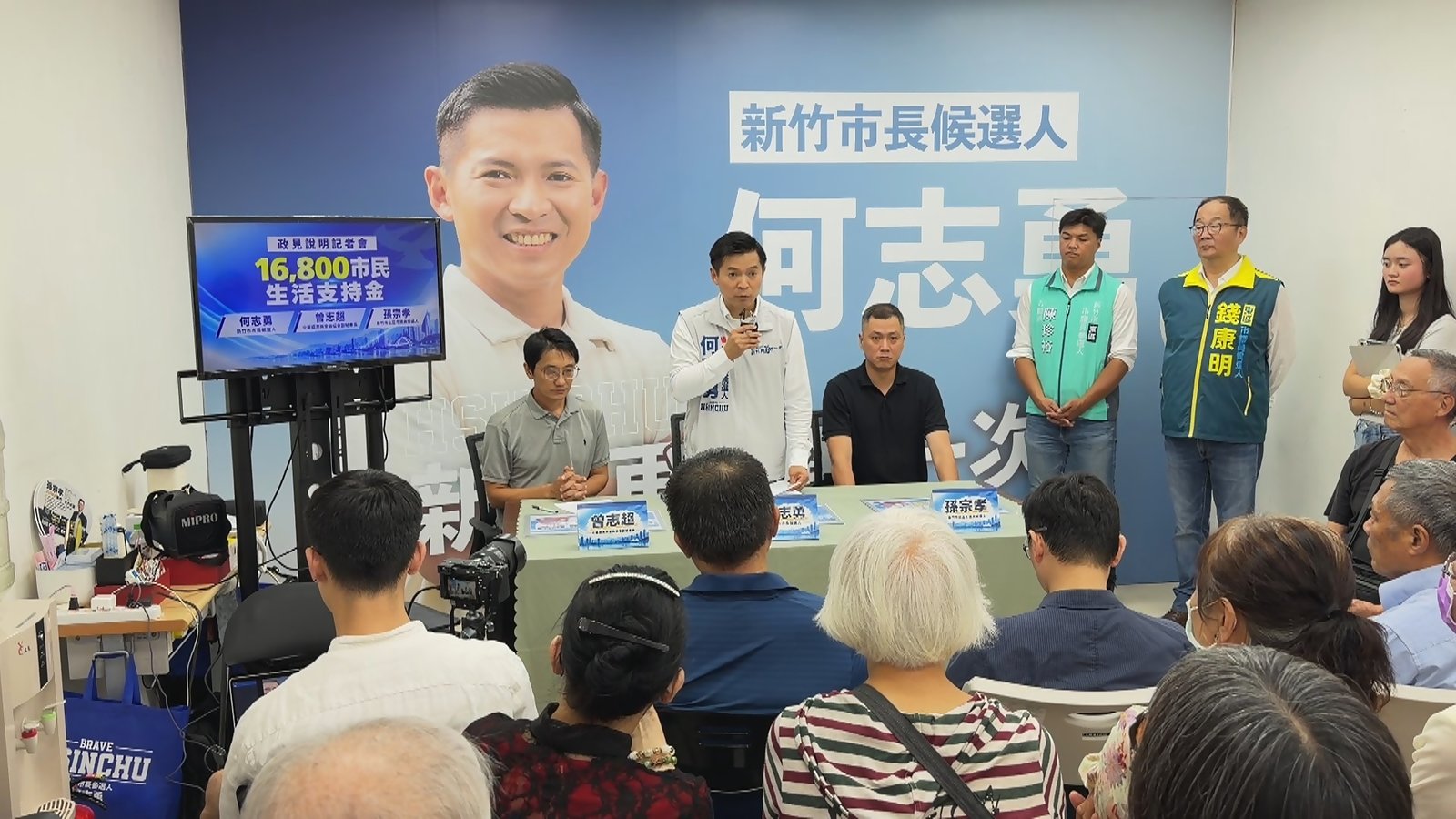 新竹市長候選人何志勇(中)30日在競選總部政見說明記者會提出16,800市民生活支持金。(新唐人亞太電視)